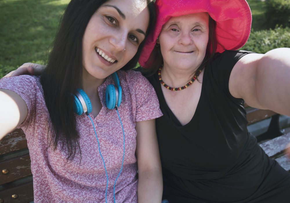 Woman with Down Syndrome and her assistant  making selfie in a park. Volunteering and community service.