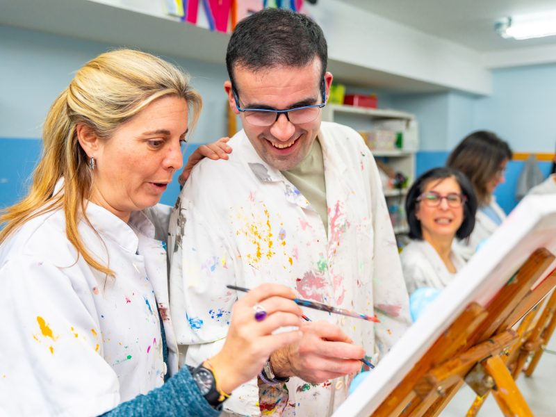 Instructor helping a disabled man during painting class in a center for people with special needs